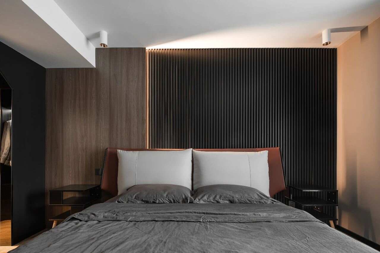 床上铺设着灰色皮革床垫和灰色床单。床头墙采用米白色硬包装饰材料，使整个卧室呈现出现代简约而舒适的感觉。